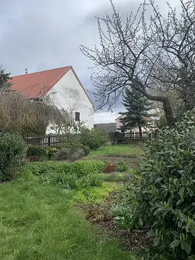 Blick auf den Garten eines Bauernhofs mit Obstbäumen, Sträuchern und einem Haus mit rotem Dach