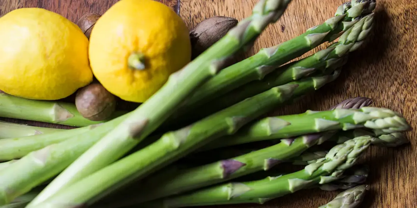 Frischer grüner Spargel mit Zitronen auf einem Holzbrett