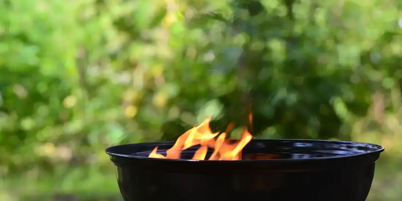 Flammen in einem schwarzen Grill vor grünem, unscharfem Hintergrund