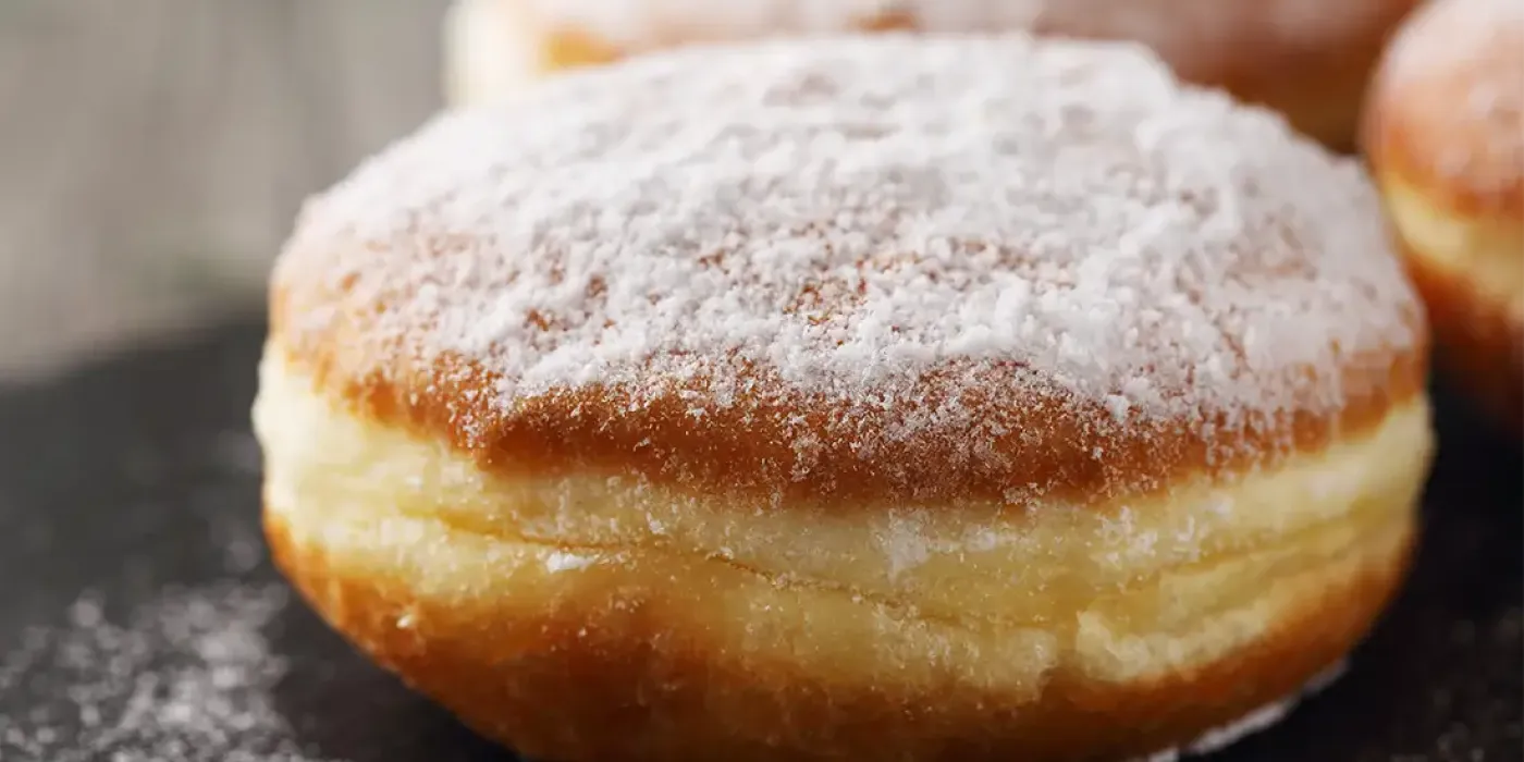 Selbstgemachter Kreppel mit Puderzucker und fruchtiger Konfitürefüllung in Nahaufnahme