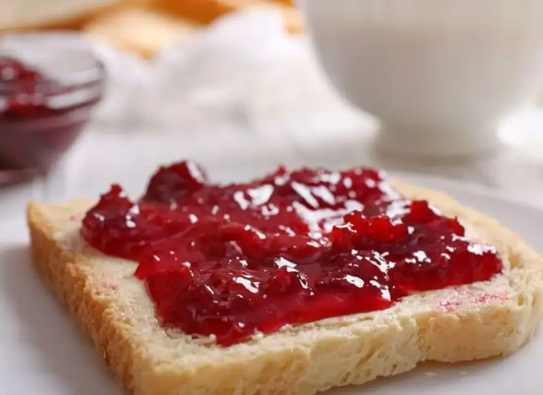 Weißbrotscheibe mit roter Erdbeer- oder Himbeermarmelade auf Teller