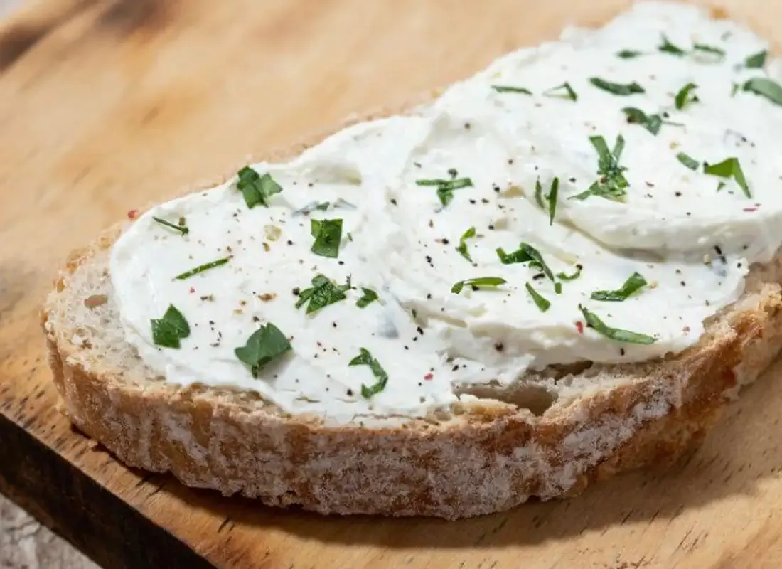 Rustikale Brotscheibe mit veganem Frischkäse und frischen Kräutern