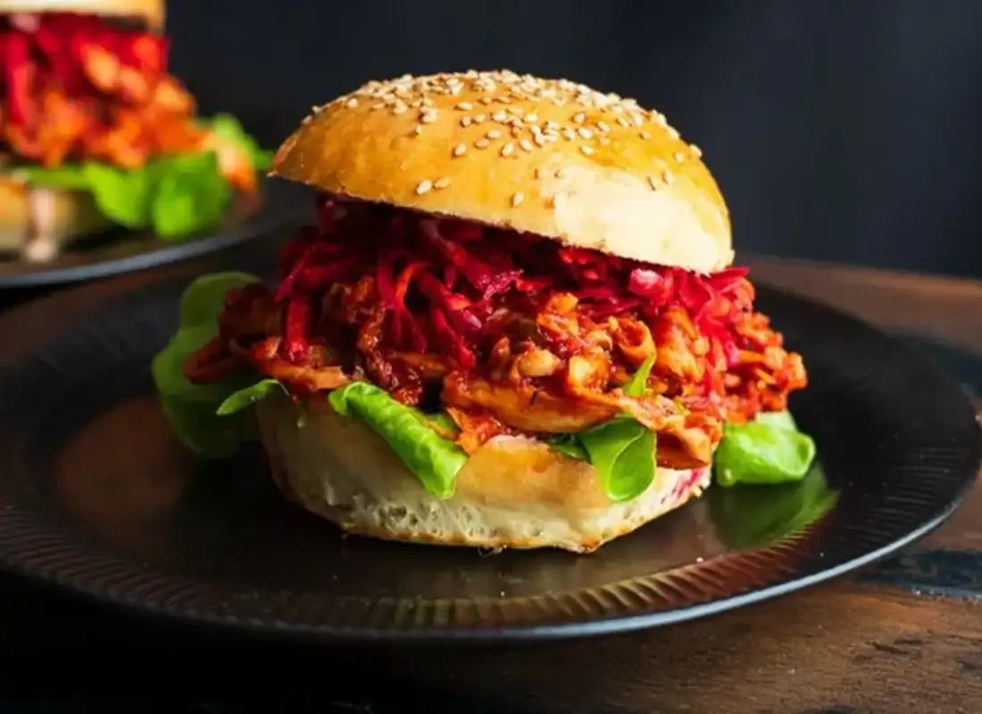 Nahaufnahme eines veganen Pulled-Pilz-Burgers mit Salat und Rote-Bete-Topping im Sesam-Bun