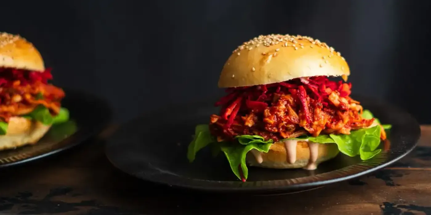 Veganer Pulled-Pilz-Burger mit Salat, Rote-Bete-Streifen und Sesam-Bun auf dunklem Teller